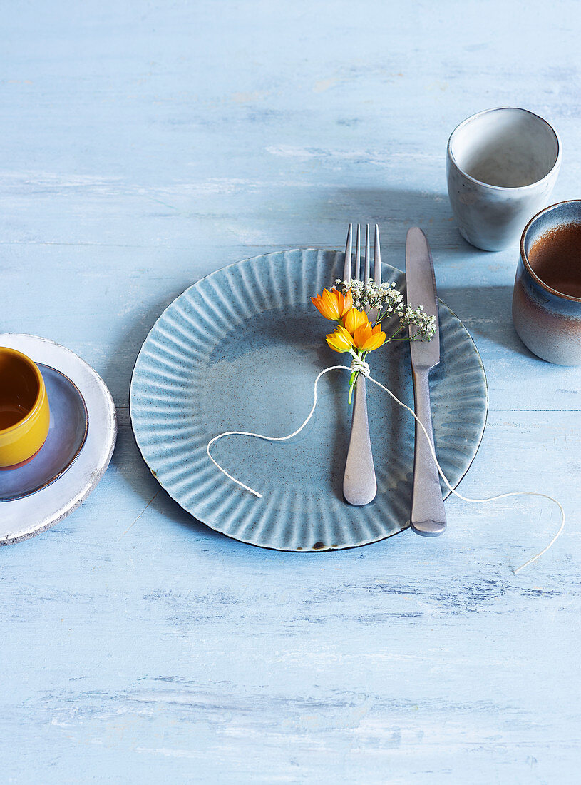 A blue plate with a knife and fork next to an earthenware cup and mug