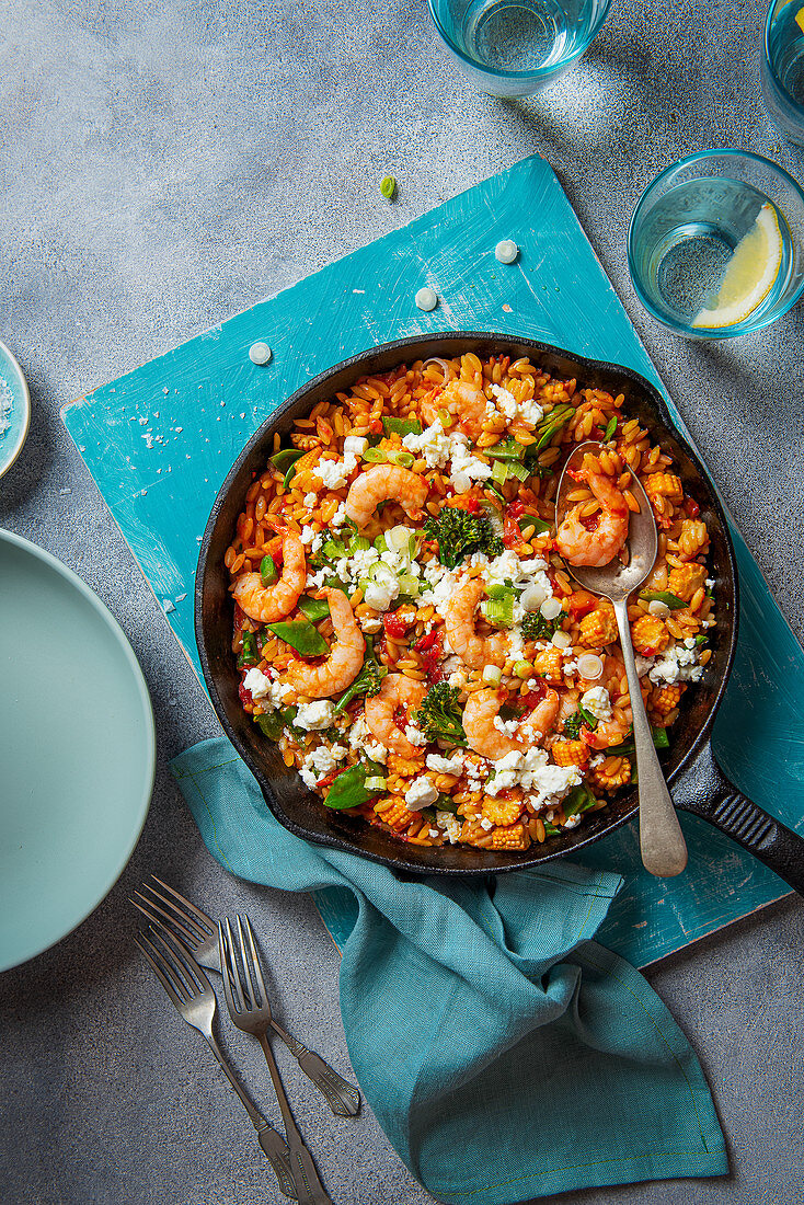 Orzo pasta cooked in tomato sauce with king prawns, vegetables and crumbled feta cheese
