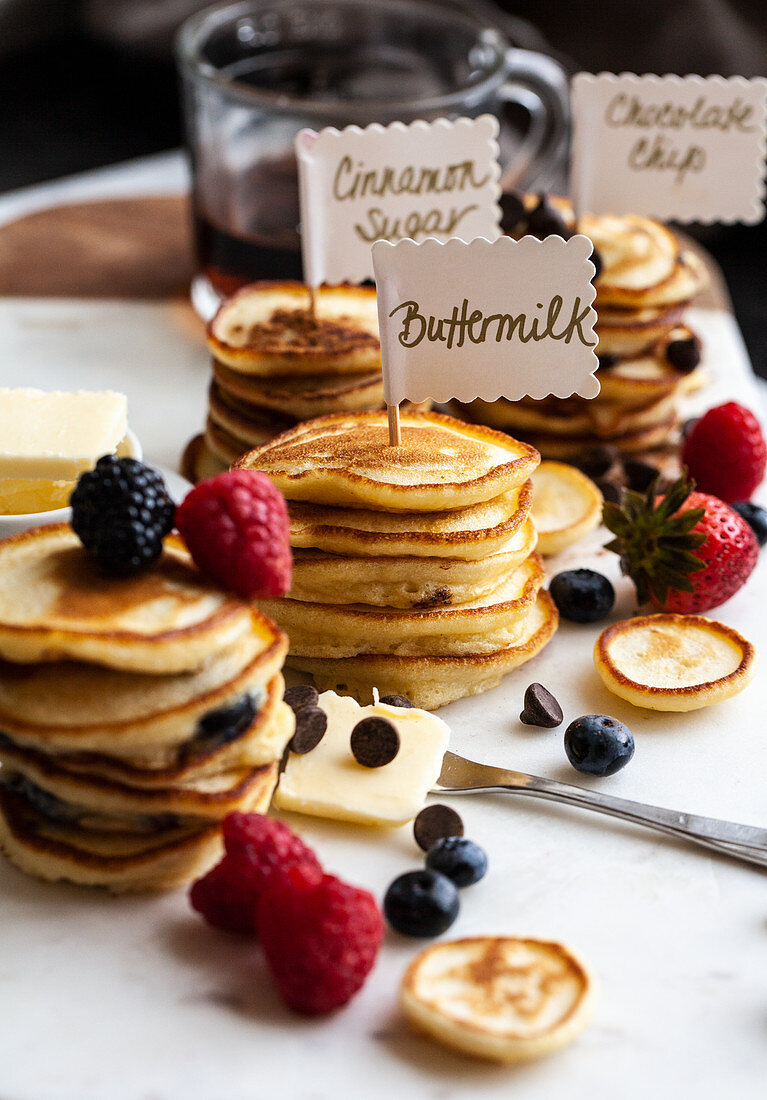 Stapel von Mini Pancakes mit Schildern, Beeren, Butter und Schokoladenstückchen