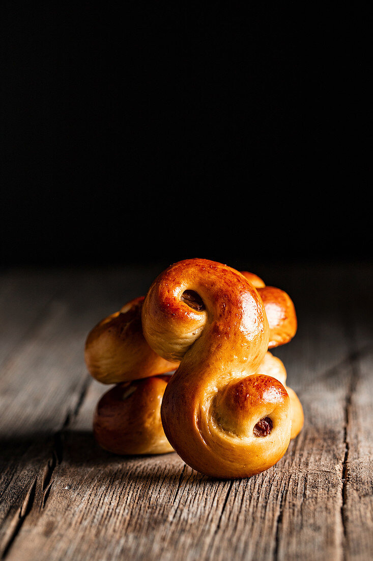 Delicious fresh baked traditional saffron buns with raisin placed on wooden table against black background