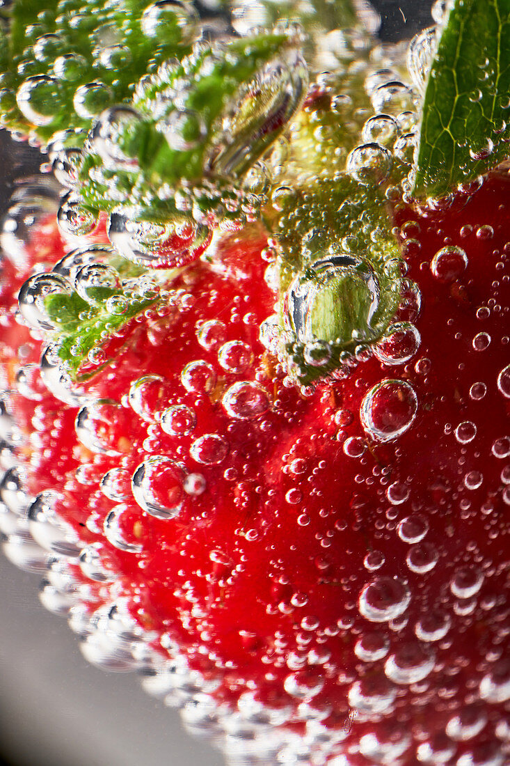 Closeup ripe red strawberry covered with air bubbles floating in transparent clear water
