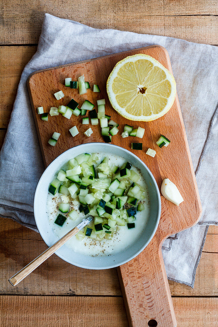 Bowl with delicious cold cucumber and yogurt tarator soup with garlic and lemon served on wooden table