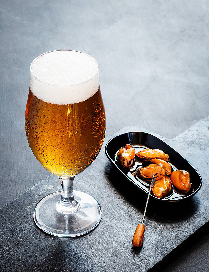 Fresh beer served with marinated mussels on dark background