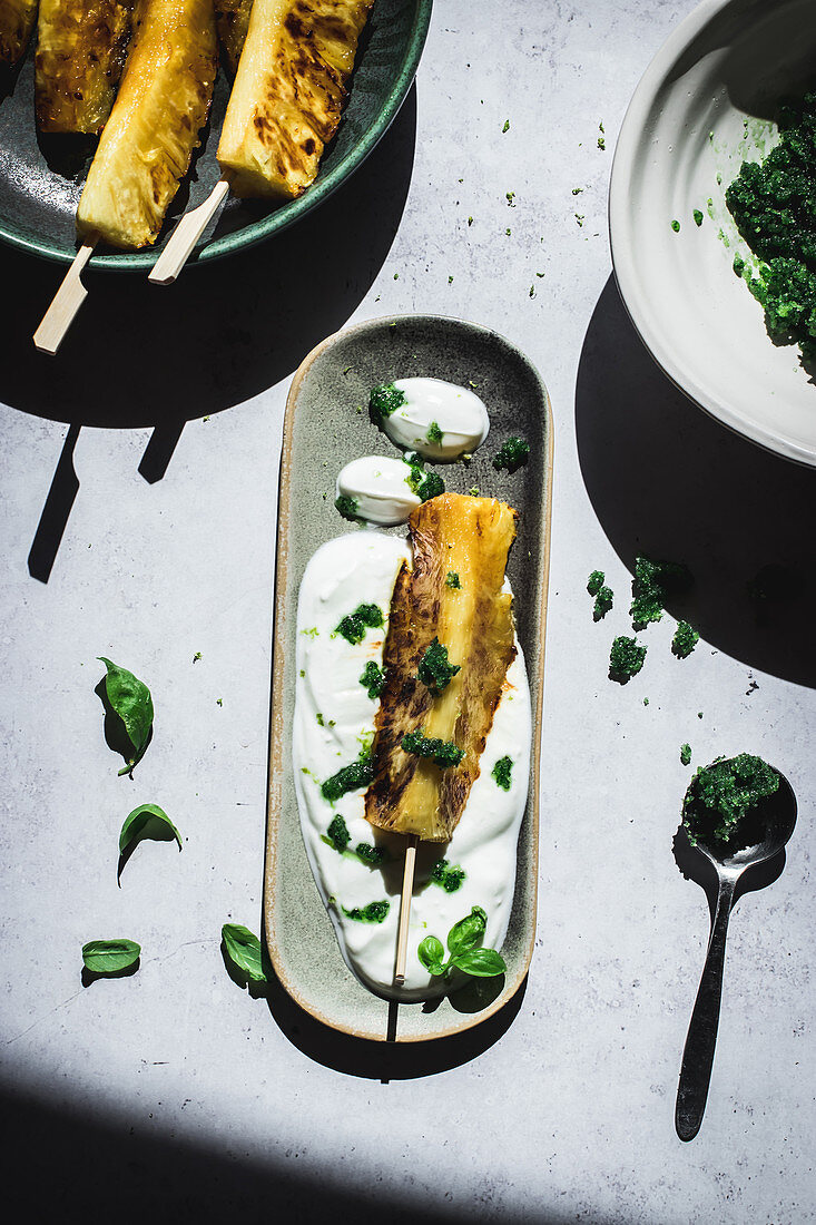 Roasted pineapple served with fresh yogurt and basil sugar on table with shadows