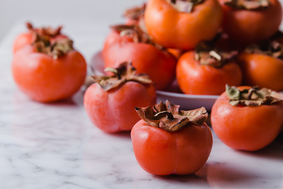 Pile of fresh persimmons on plate placed on white table