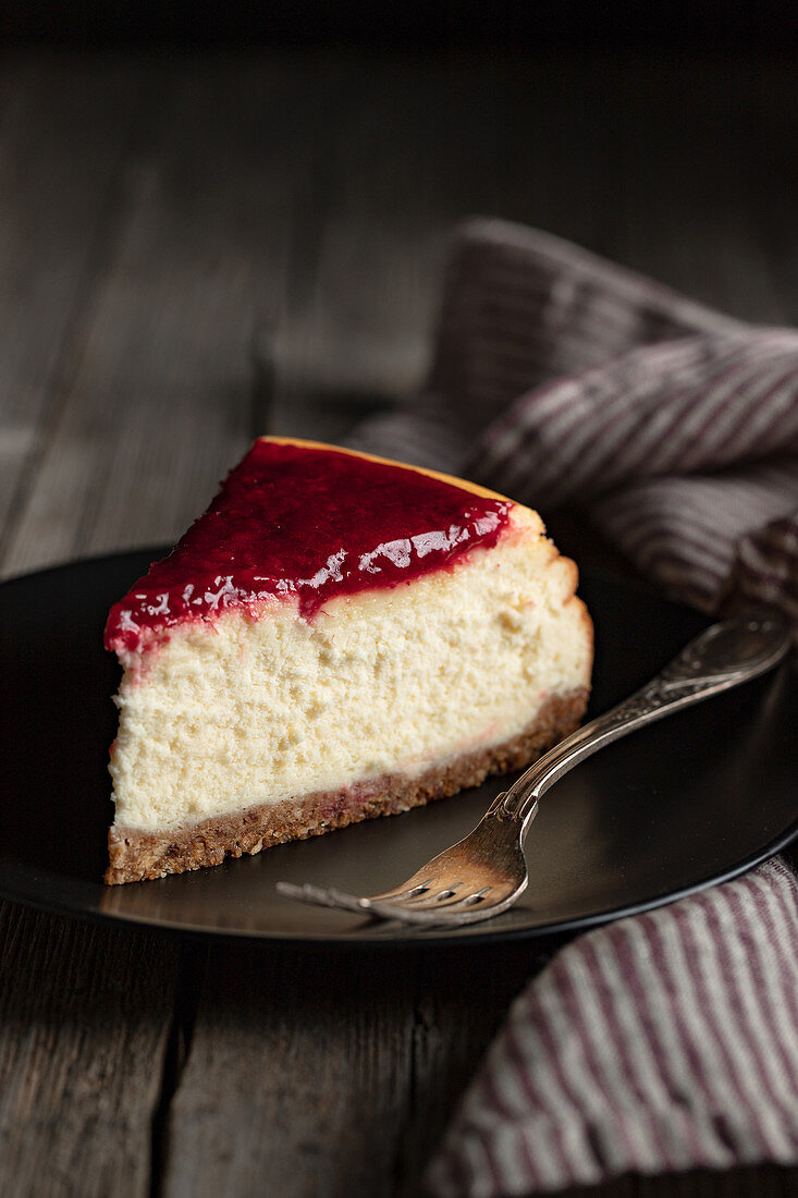 Delicious homemade cheesecake with red berry jam served on black plate on wooden table