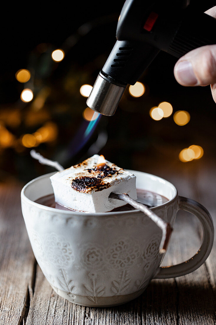 Kitchen burner roasting marshmallow on stick over cup of hot chocolate