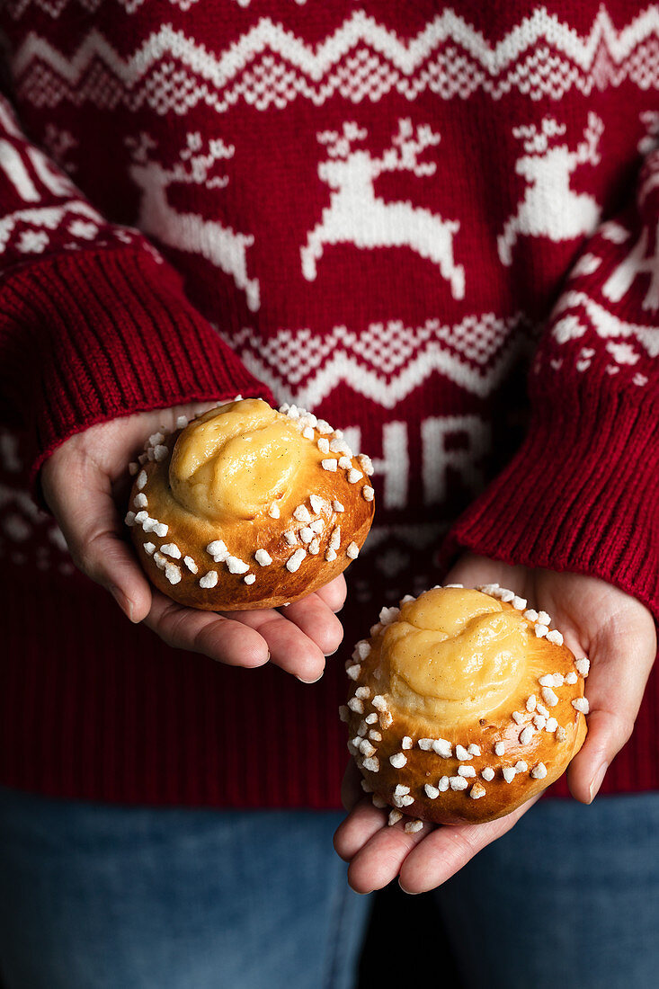 Crop female in red christmas sweater and jeans holding homemade tasty fresh buns with white sprinkles