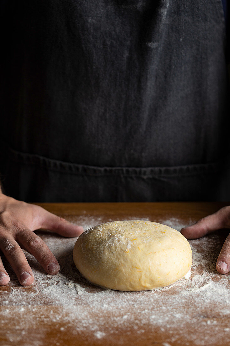 Forming artisan round bread loaf while standing at wooden table dusted with white flour