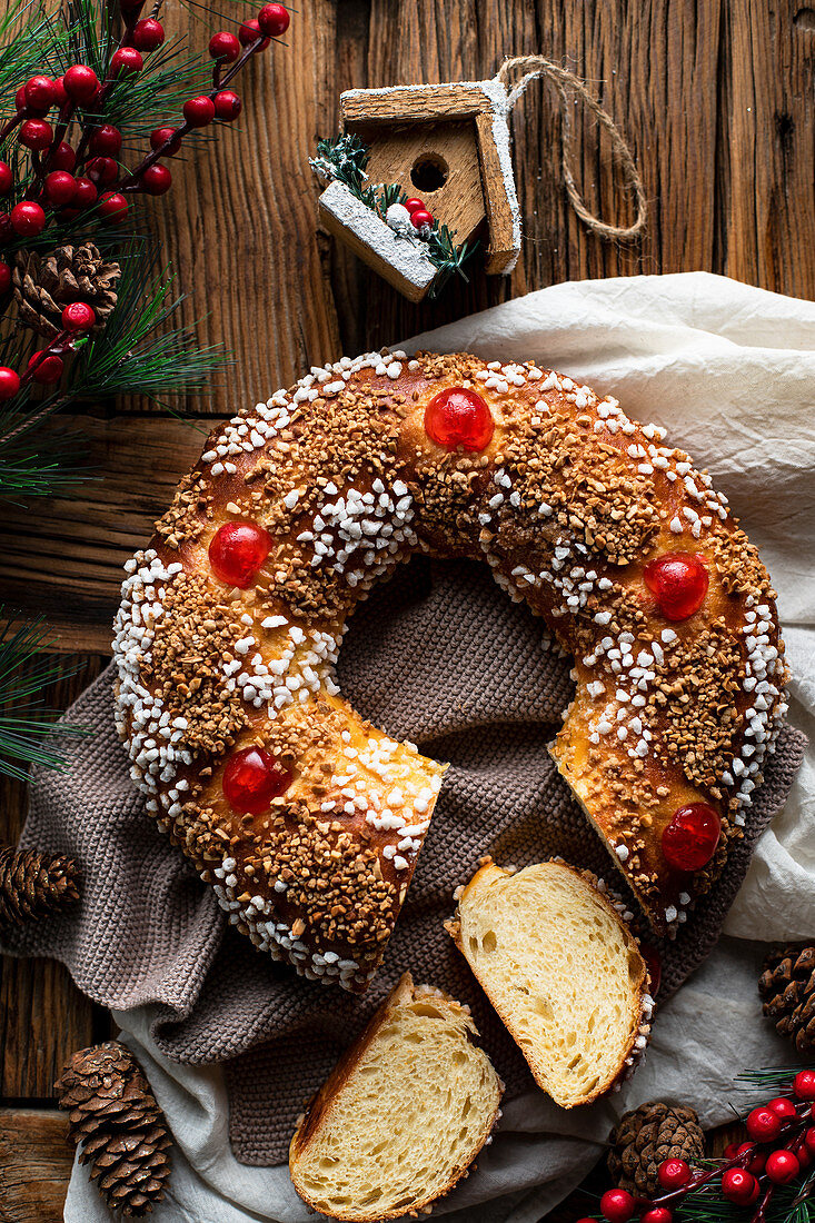 Homemade round bread with hole decorated with sprinkles and cherry placed on wooden table with Christmas decoration