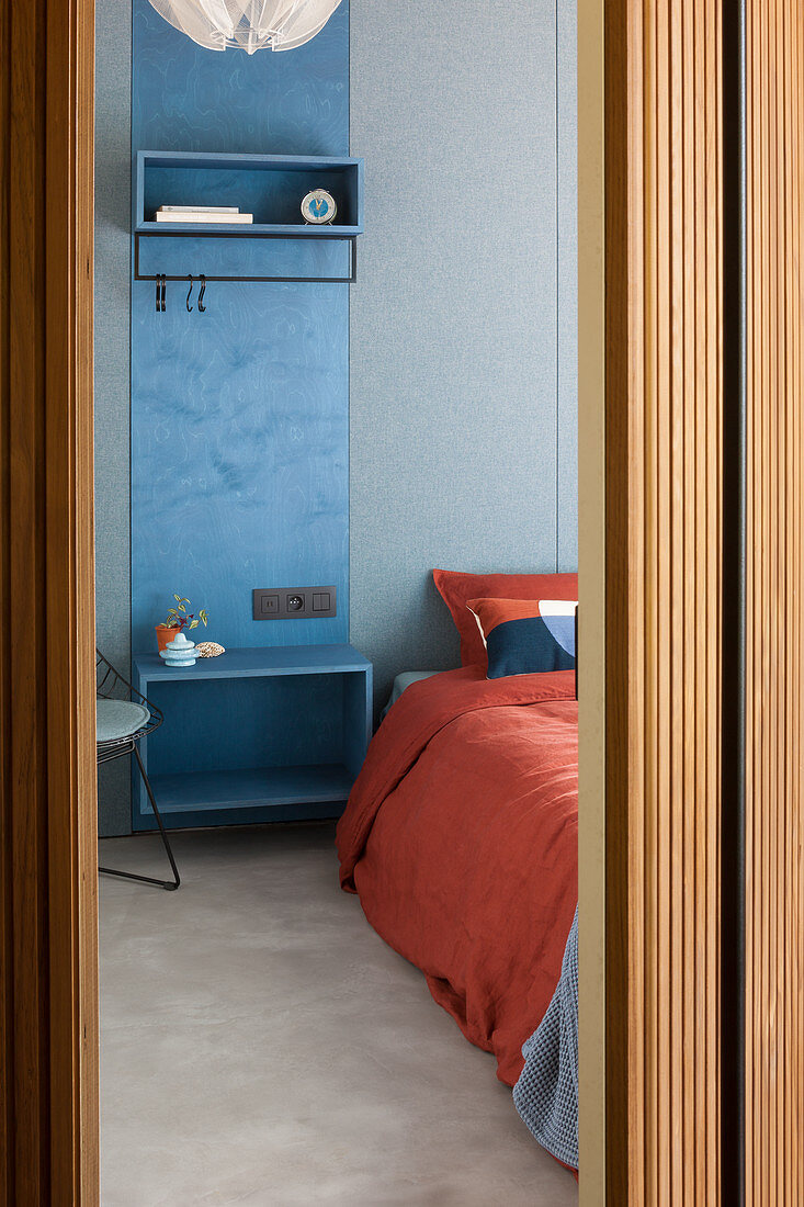 Blick auf blaues Garderobenpaneel als Nachttisch neben Bett