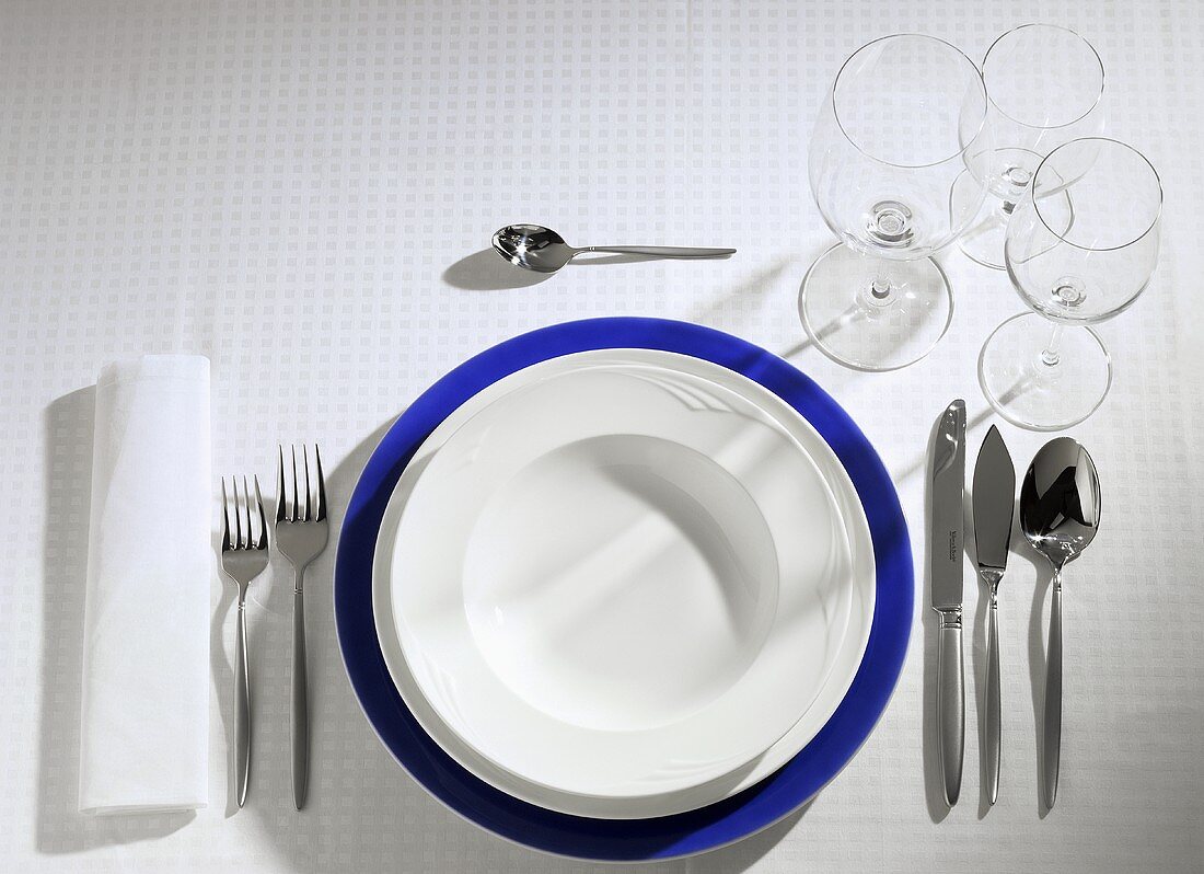 Table setting: blue, white & soup plate, cutlery, wine glasses