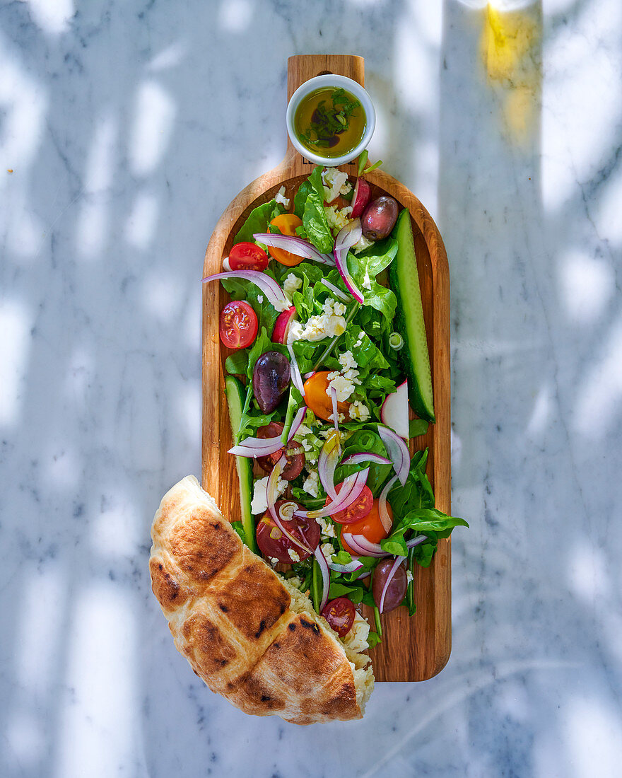 Griechischer Salat serviert mit Fladenbrot und Vinaigrette auf Holzbrett