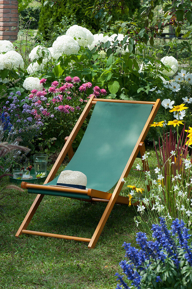 Folding deck chair on a small lawn island between flowering shrubs and hydrangeas shrub