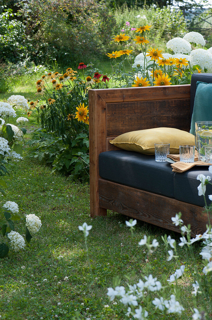 Sofa im Garten zum draußen wohnen im Sommer, umgeben von Sonnenhut und Strauchhortensien