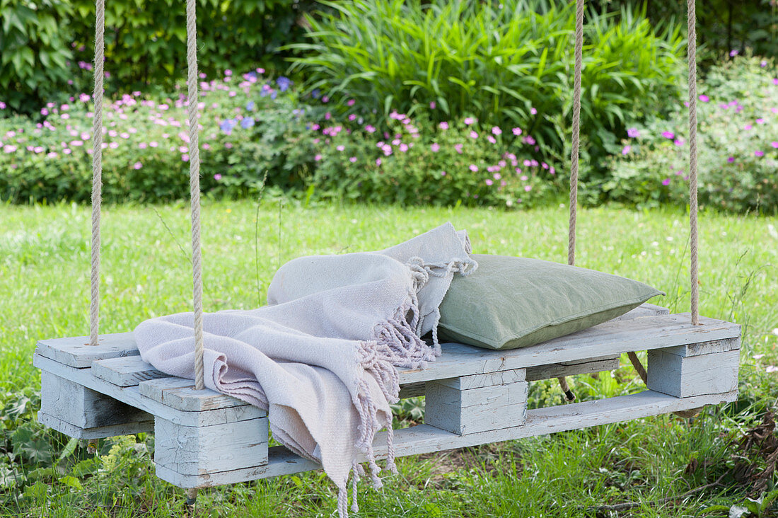 White pallet as a seat hung on a tree with ropes, blanket and pillow