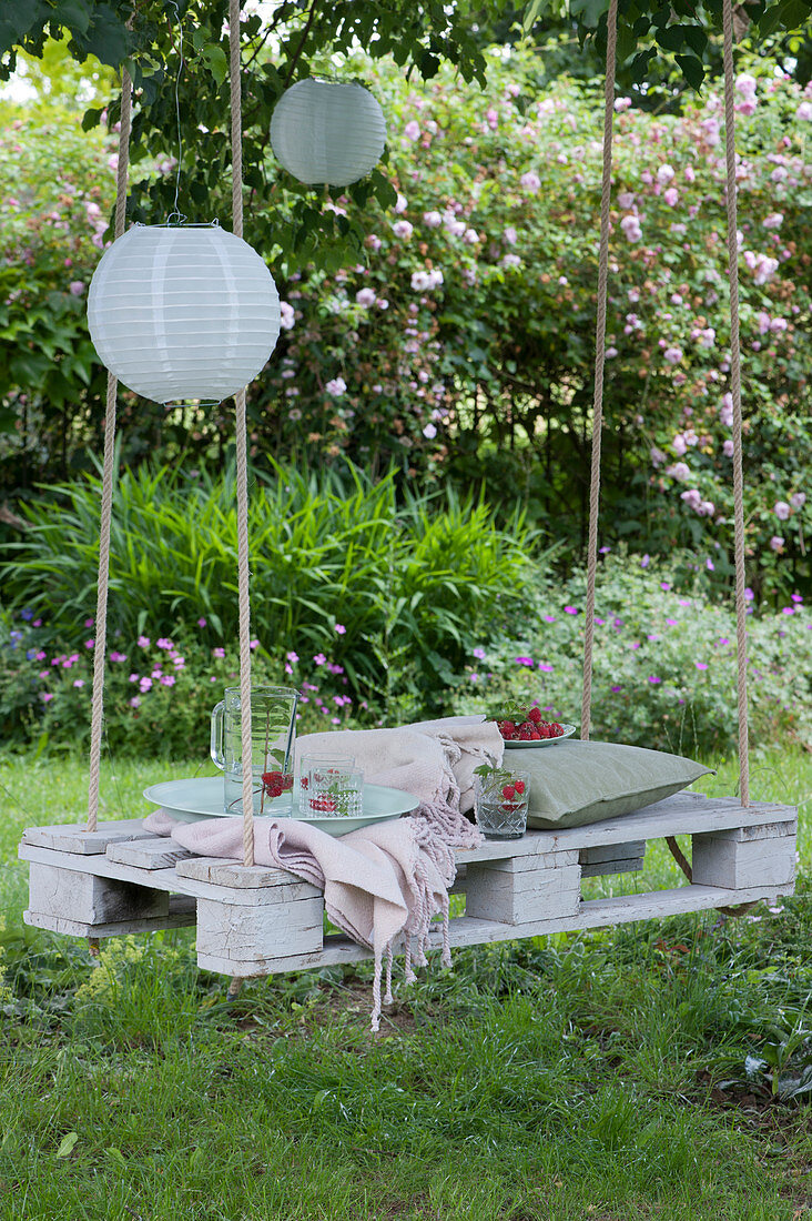 White pallet as a seat hung from a tree with ropes, paper lanterns, jug with water, mint and raspberries