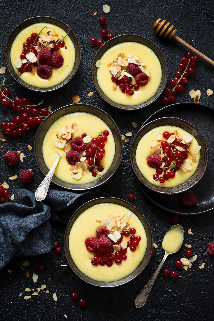 Orange millet pudding in bowls with red currants and raspberries