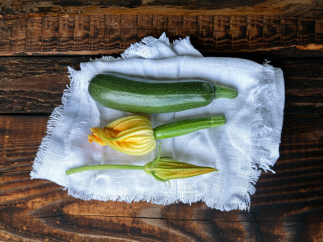Fresh green zucchini and zucchini flowers on a linen cloth