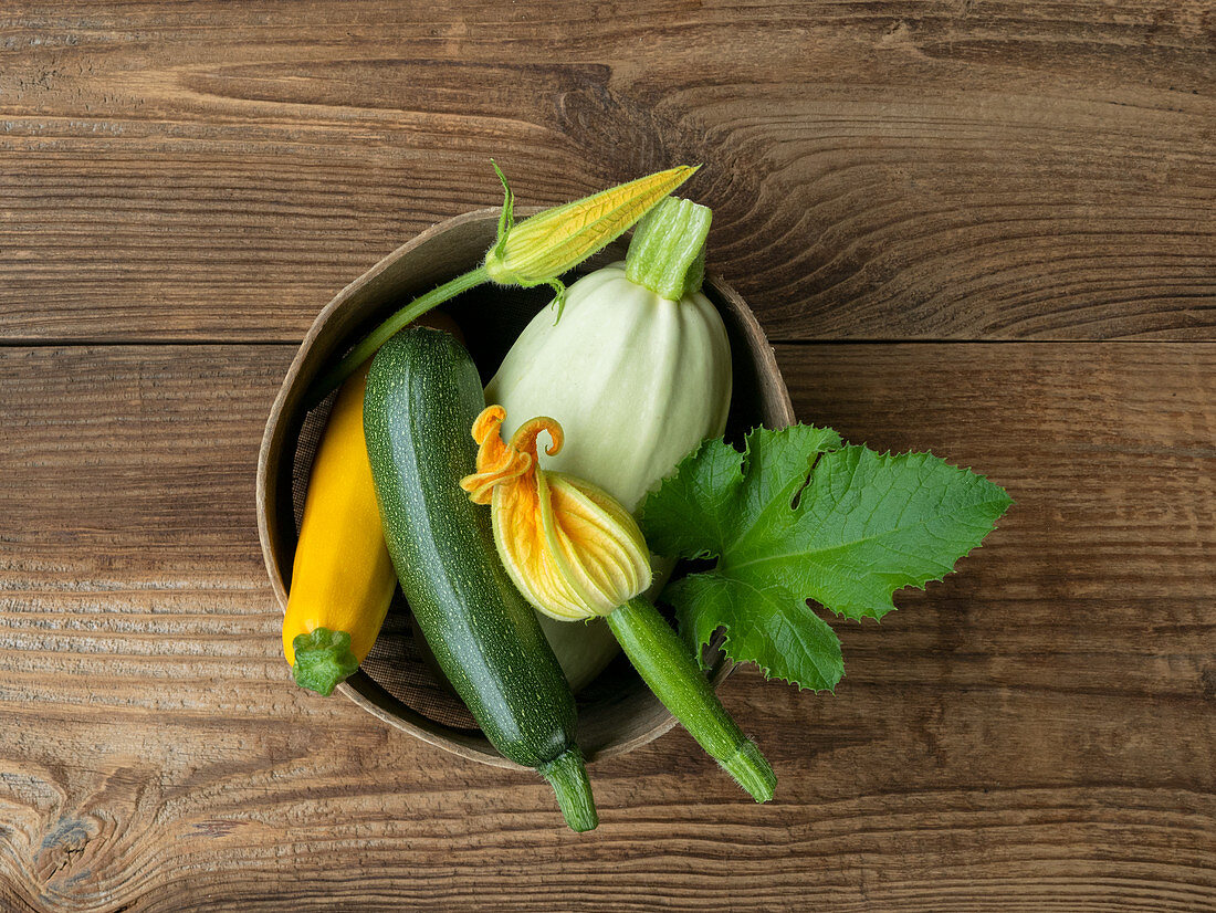 Various fresh zucchini and zucchini flowers in a bowl