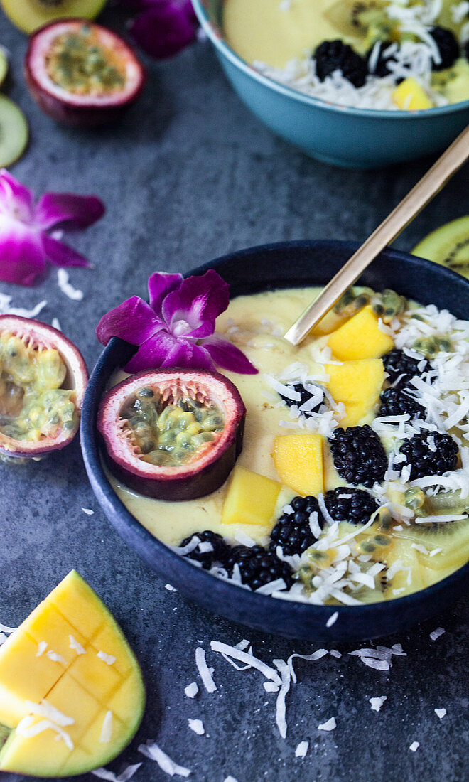Mango smoothie bowl topped with passion fruit, an orchid, blackberry, yellow kiwi and coconut