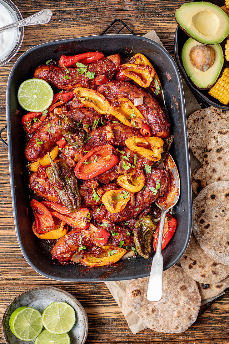 Wurstauflauf mit Mini-Paprika serviert mit Tortillas, Avocado und Mais