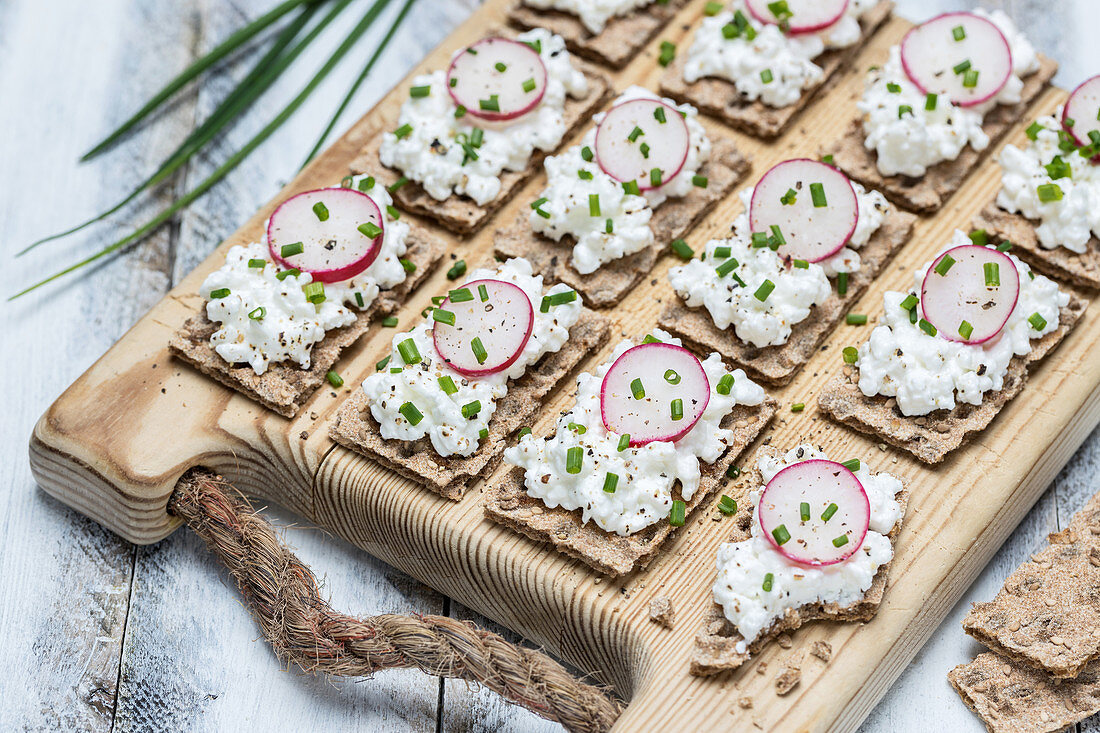 Knäckebrotscheiben mit Hüttenkäse und Radieschen auf Holzbrett