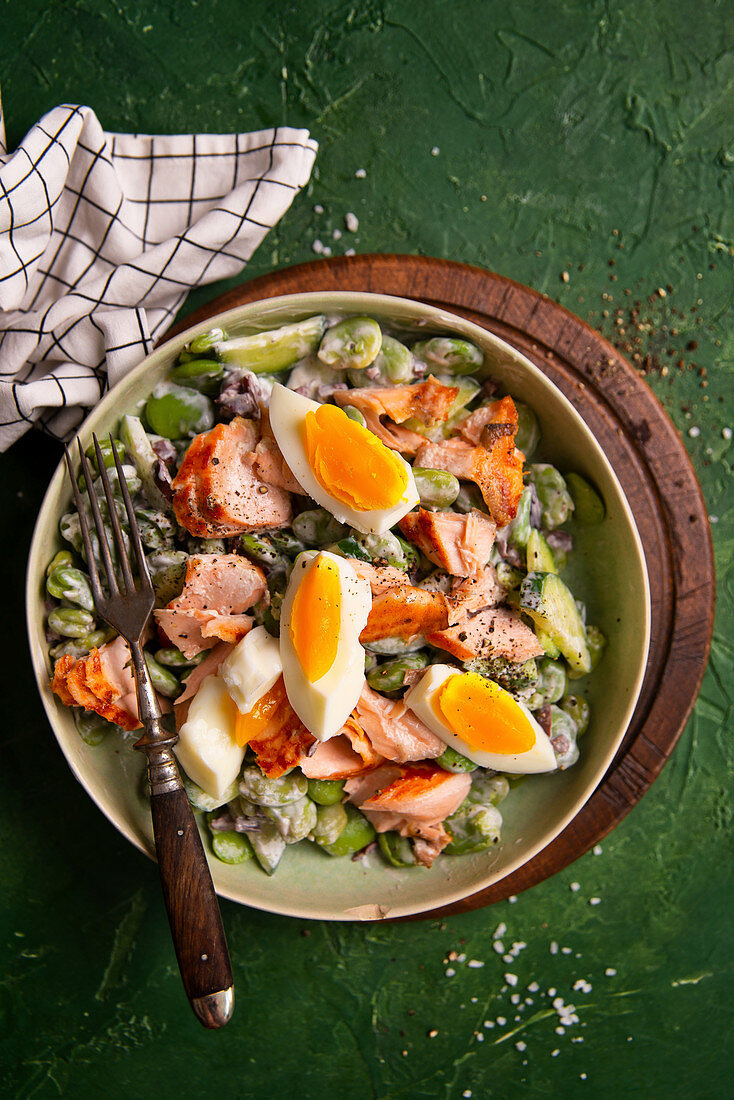 Salat mit Saubohnen, Gurken, Oliven, Lachs, Ei und griechischem Joghurtdressing