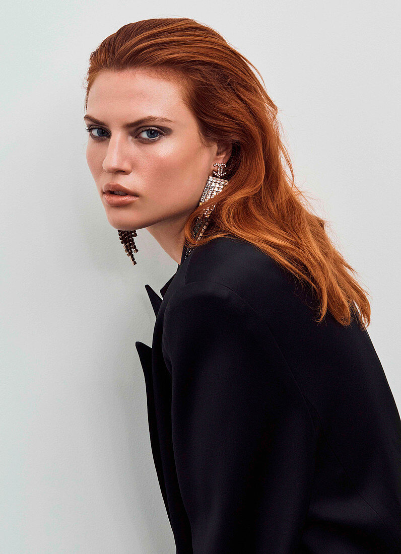 A red-haired woman wearing earrings and a black blazer