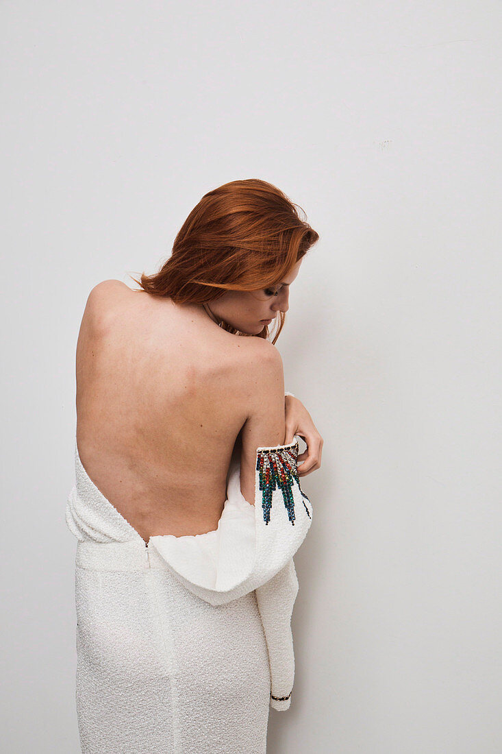 A red-haired woman wearing a white designer dress embroidered with rhinestones