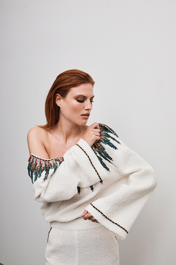 A red-haired woman wearing a white designer dress embroidered with rhinestones