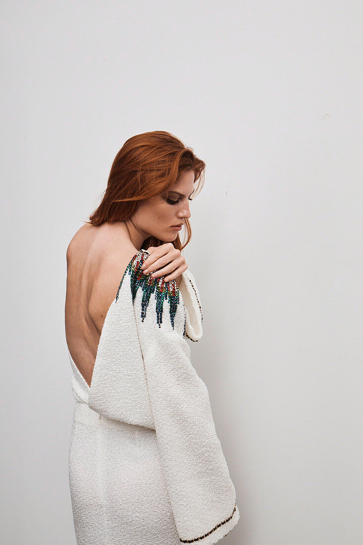 A red-haired woman wearing a white designer dress embroidered with rhinestones