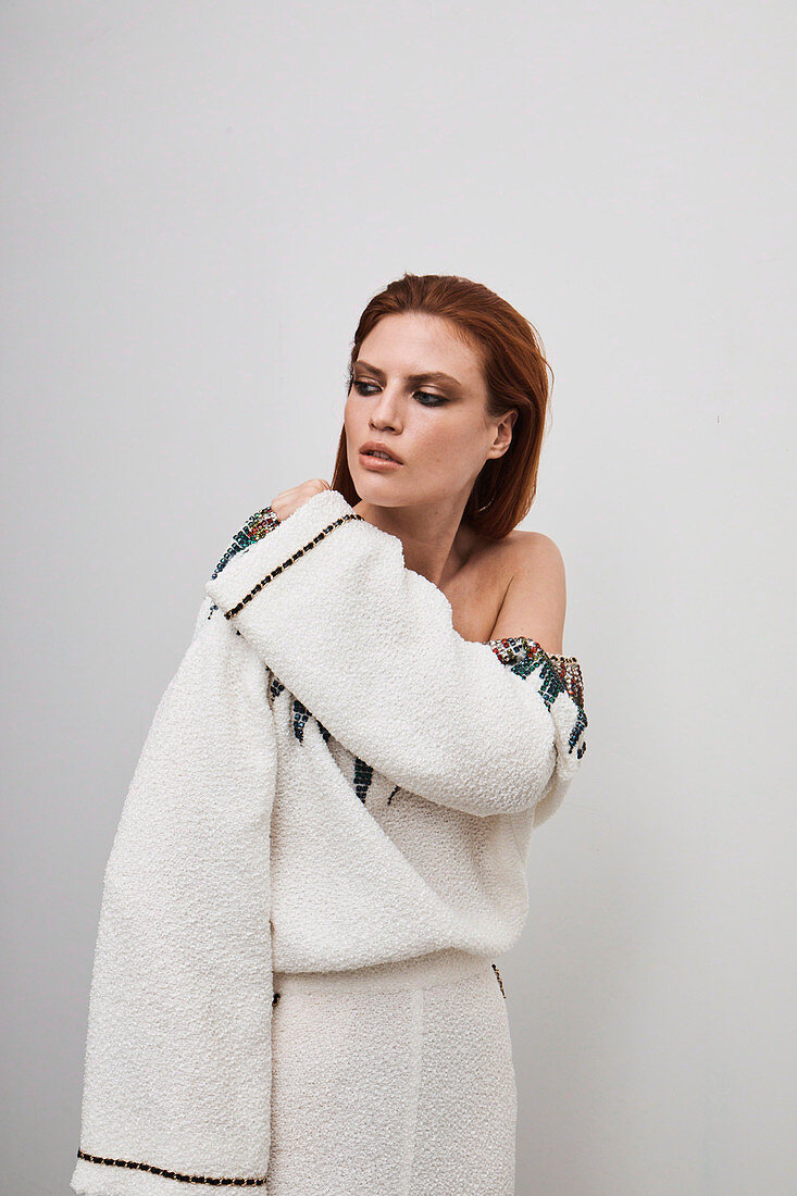 A red-haired woman wearing a white designer dress embroidered with rhinestones