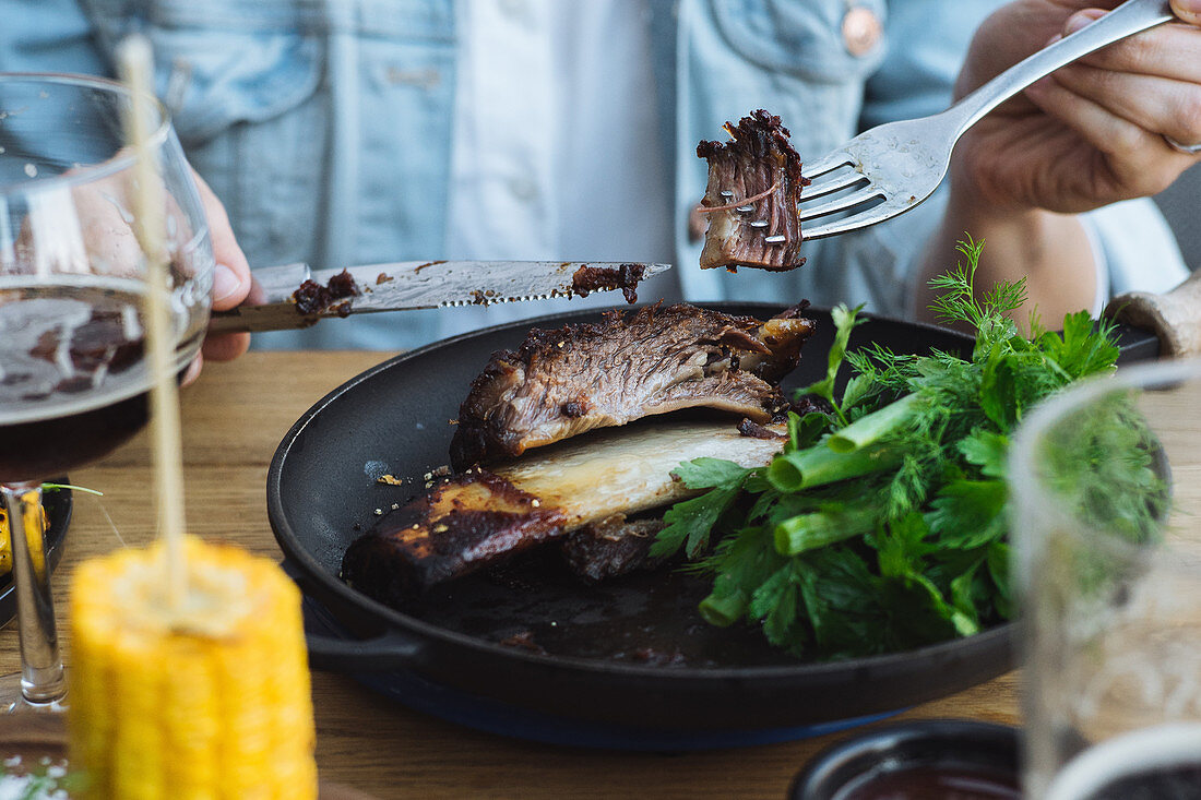 Eating delicious grilled beef steak with bone served with fresh greenery and grilled corn