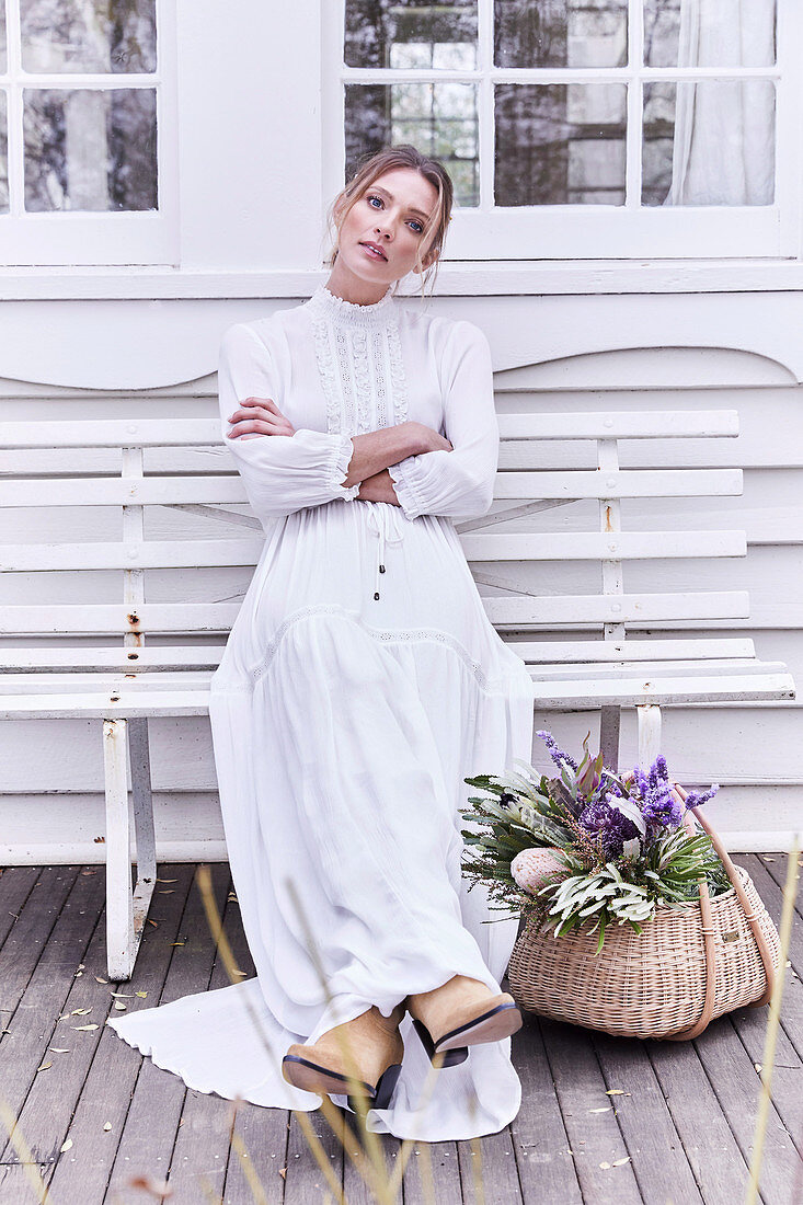 Blonde Frau in langem, weißem Kleid sitzt auf der Terrasse
