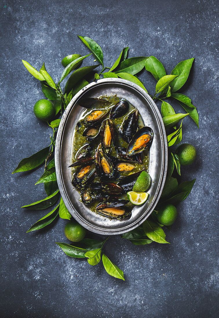 Mussels in green herb and white wine sauce with lemon on dark background