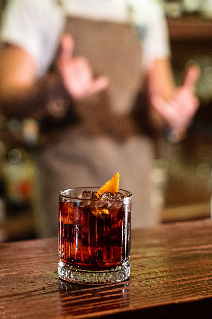 Cold alcohol cocktail with orange peel garnish and ice cubes