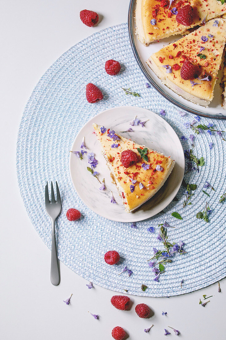 Sliced homemade raspberry baked cheesecake on plate decorated by fresh raspberries, edible flowers and mint