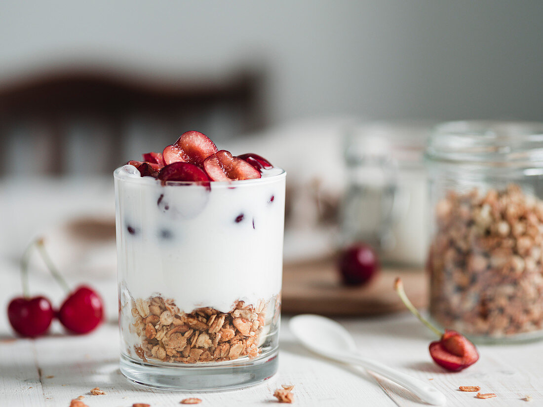 Fermented probiotic kefir or yogurt in glass with granola at the bottom served fresh sweet cherry halves