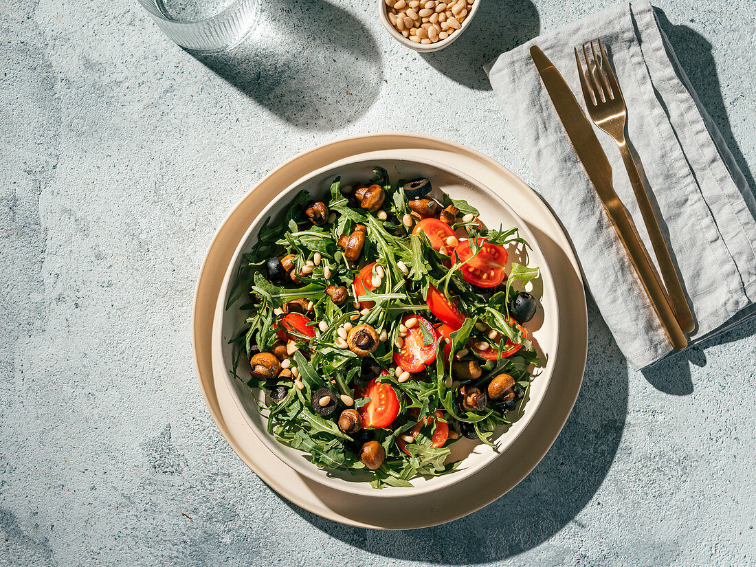 Rucolasalat mit Mini-Champignons, Kirschtomaten, Oliven und Pinienkernen