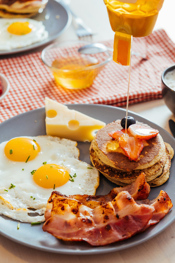 Fried eggs with cheese and bacon and pancakes with berries and honey on table for breakfast