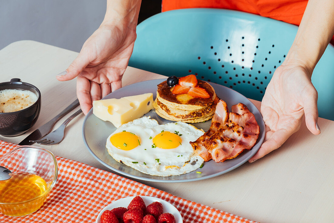 Frühstücksteller mit Pancakes, Spiegeleiern, Bacon und Käse