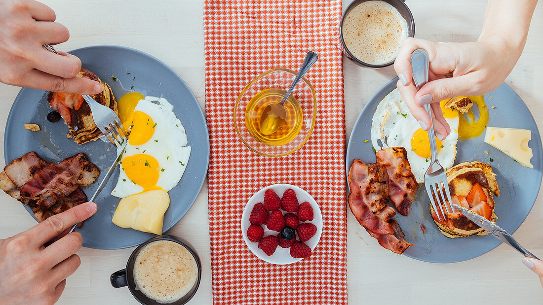 Eating tasty fried eggs with cheese and bacon and pancakes with berries for breakfast at home