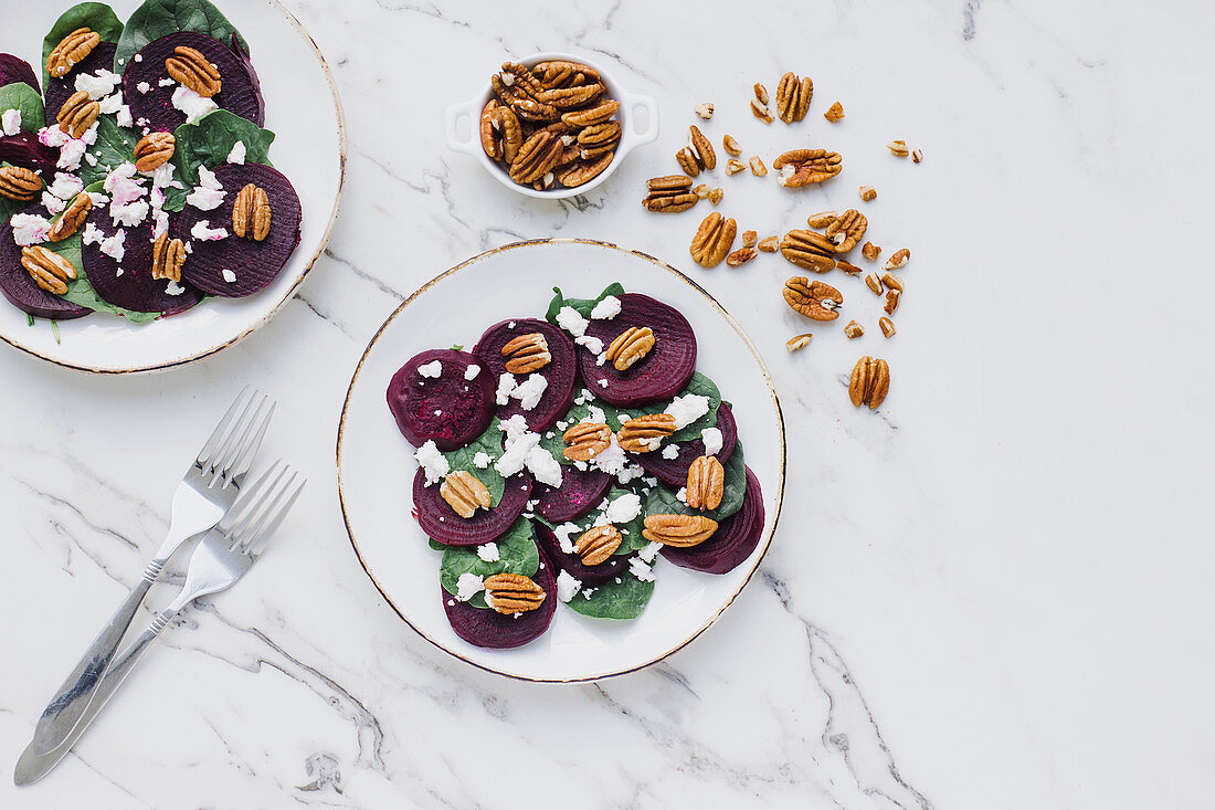 Slices of beet and spinach topped with mix of pecan nuts and goat cheese on marble table