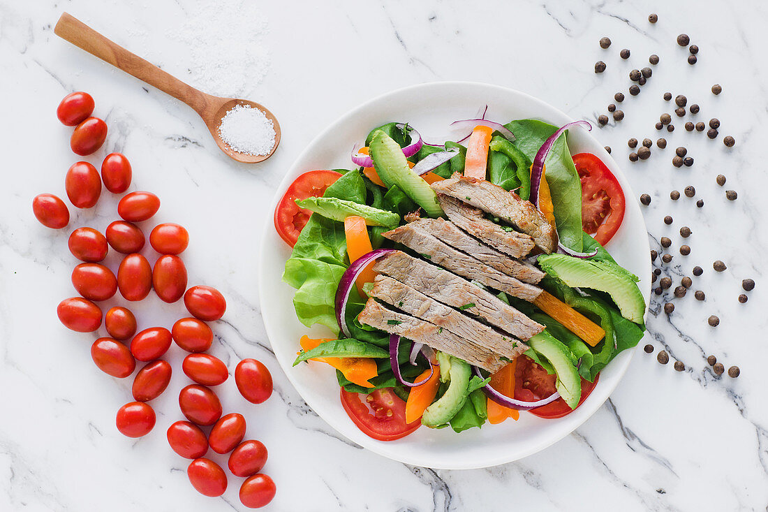 Sliced steak on pile of salad with avocado and tomatoes garnished with shopped onion