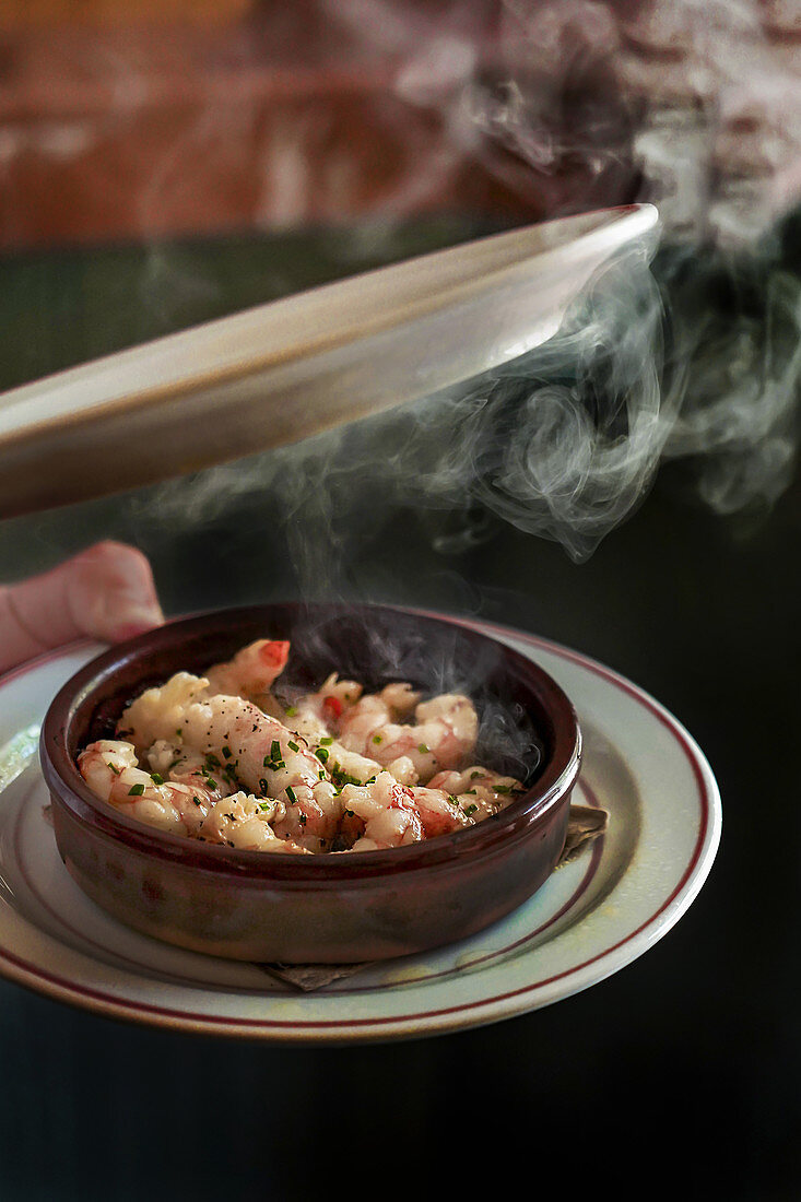 Removing plate from bowl of delicious juicy shrimps in herbs with steam coming out