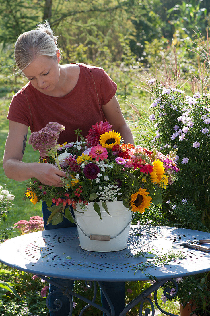 Woman puts a late summer bouquet with sunflowers, zinnias, dahlias, sedum plants, snapdragons, ornamental apples and autumn asters