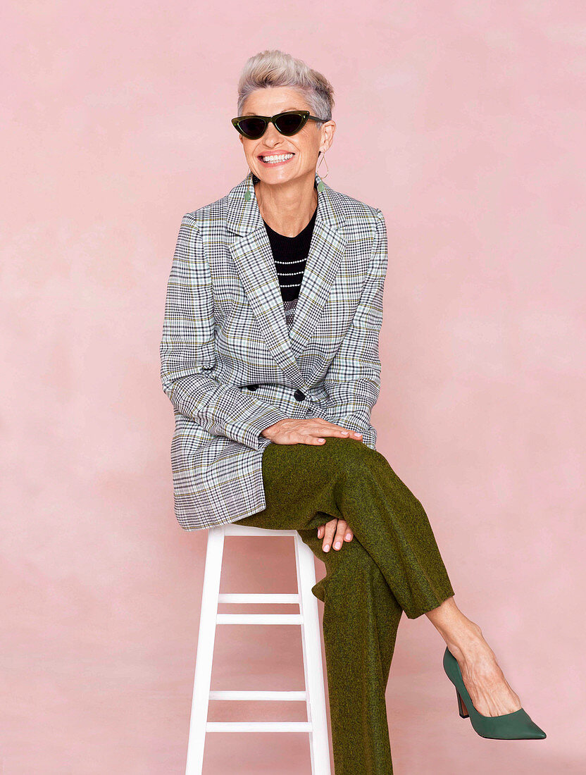 A grey-haired woman wearing a checked blazer and green trousers