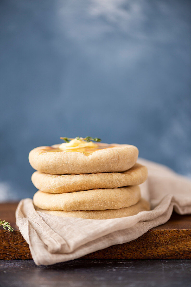 A stack of Turkish flatbread called bazlama topped with butter and thyme on a wooden board.