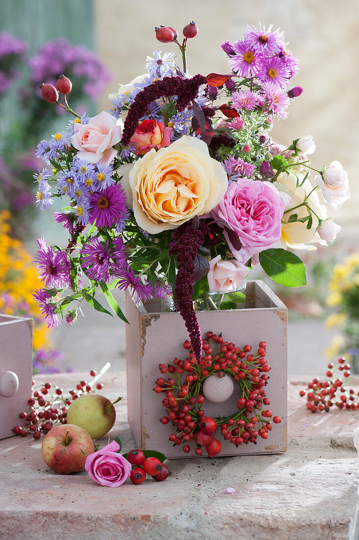 Autumn bouquet of roses, asters, rose hips and amaranth placed in an old wooden drawer, rose hips wreaths